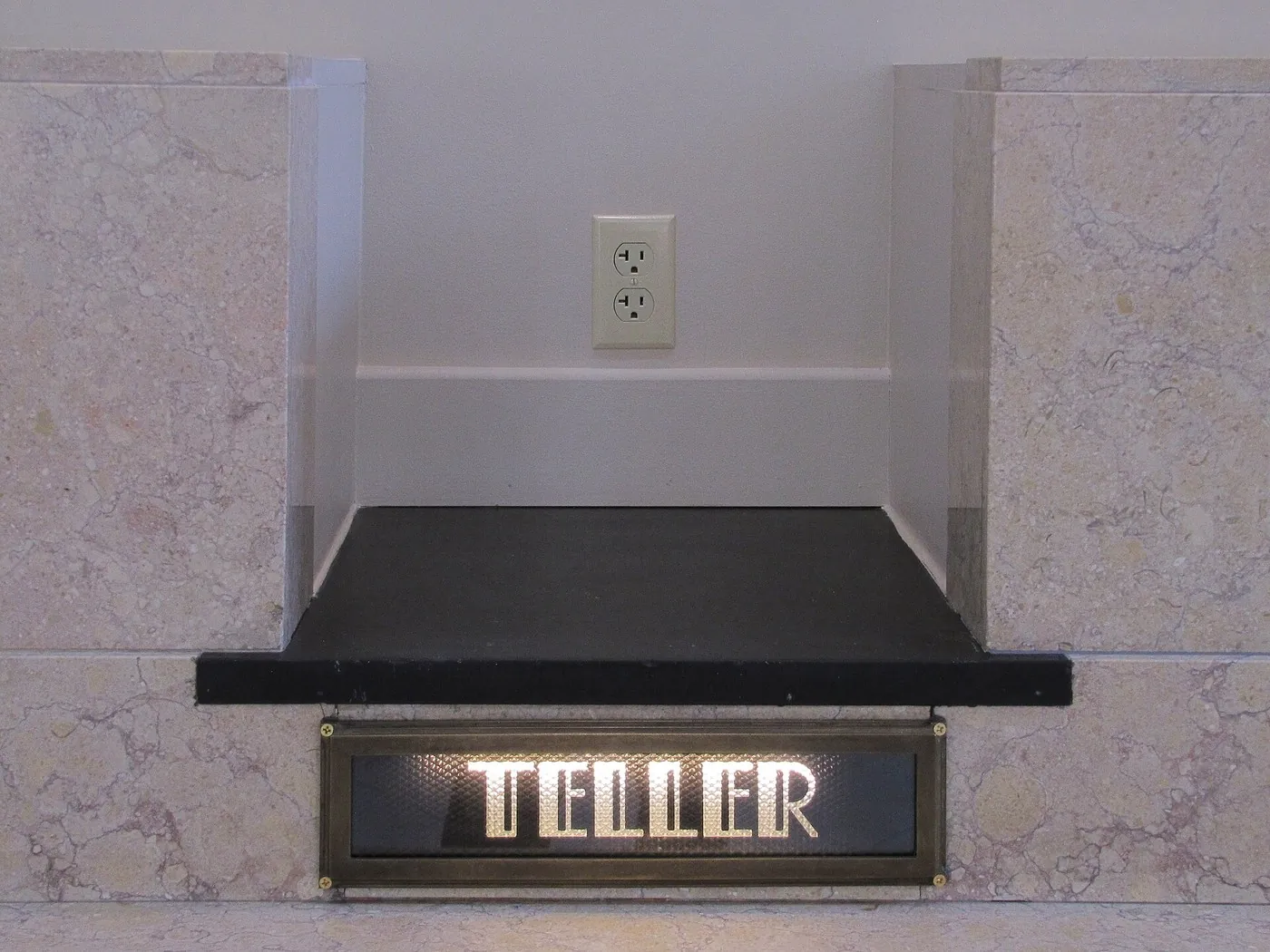 A marble teller window with a backlit TELLER sign.