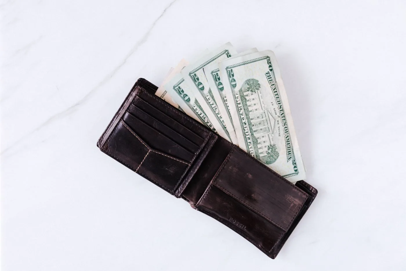 An open brown wallet with United States twenty-dollar bills on a marble surface.