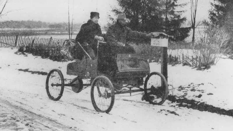 No copyright restriction A rural mail carrier in an open automobile reaching a wooden U.S. Mail box on a snowy road.