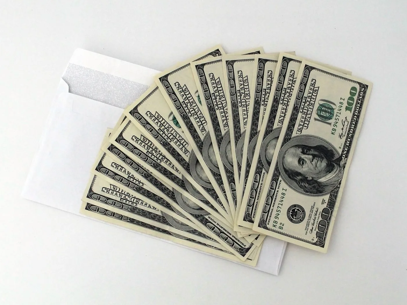 A fan of United States hundred-dollar bills resting on an open white envelope