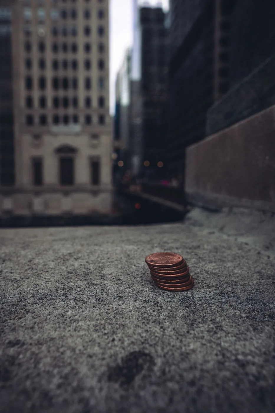 No copyright restriction A small stack of pennies on a stone ledge with city buildings behind them.