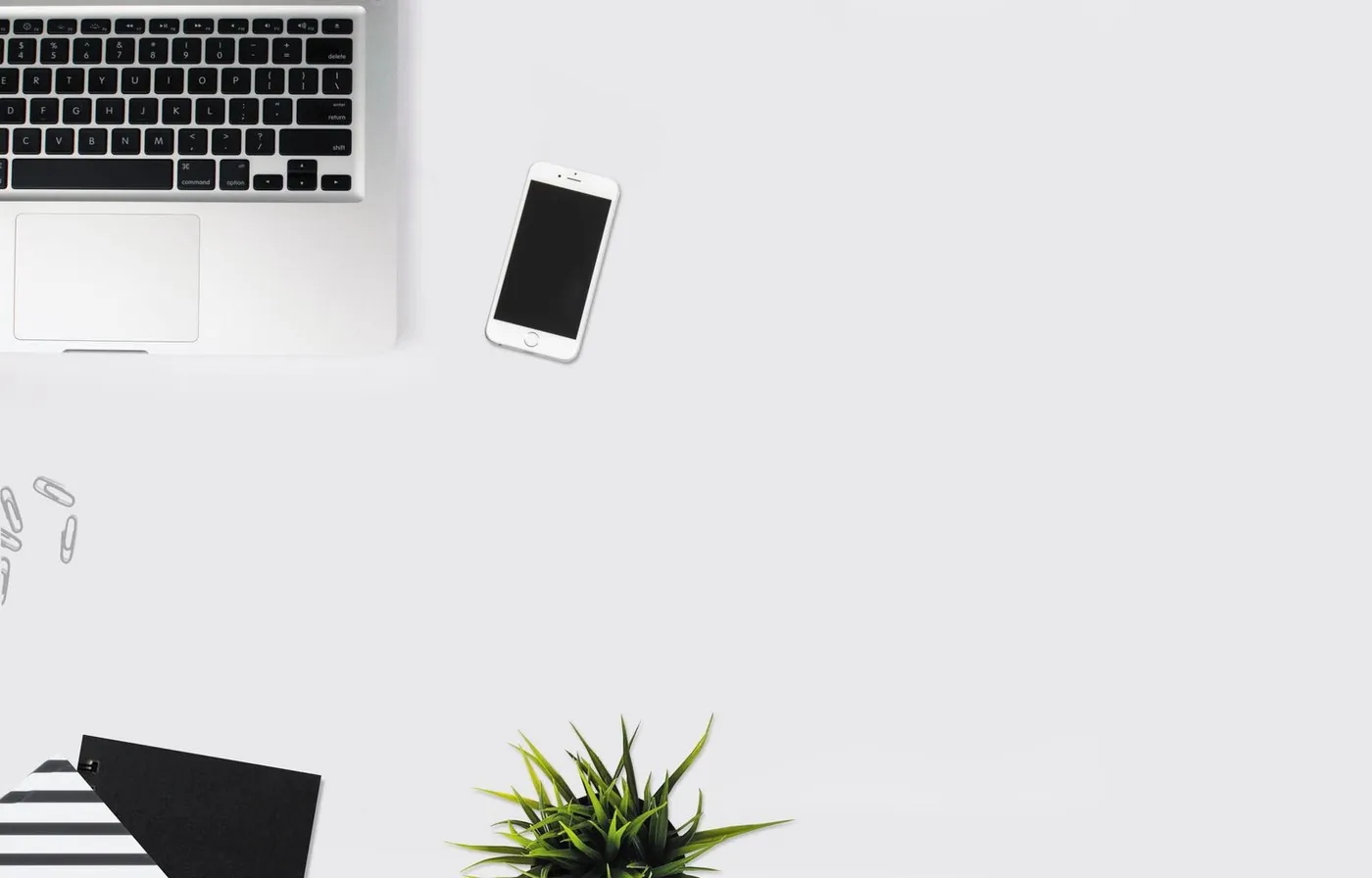 A silver laptop, a dark smartphone, and notebooks on a pale desk.
