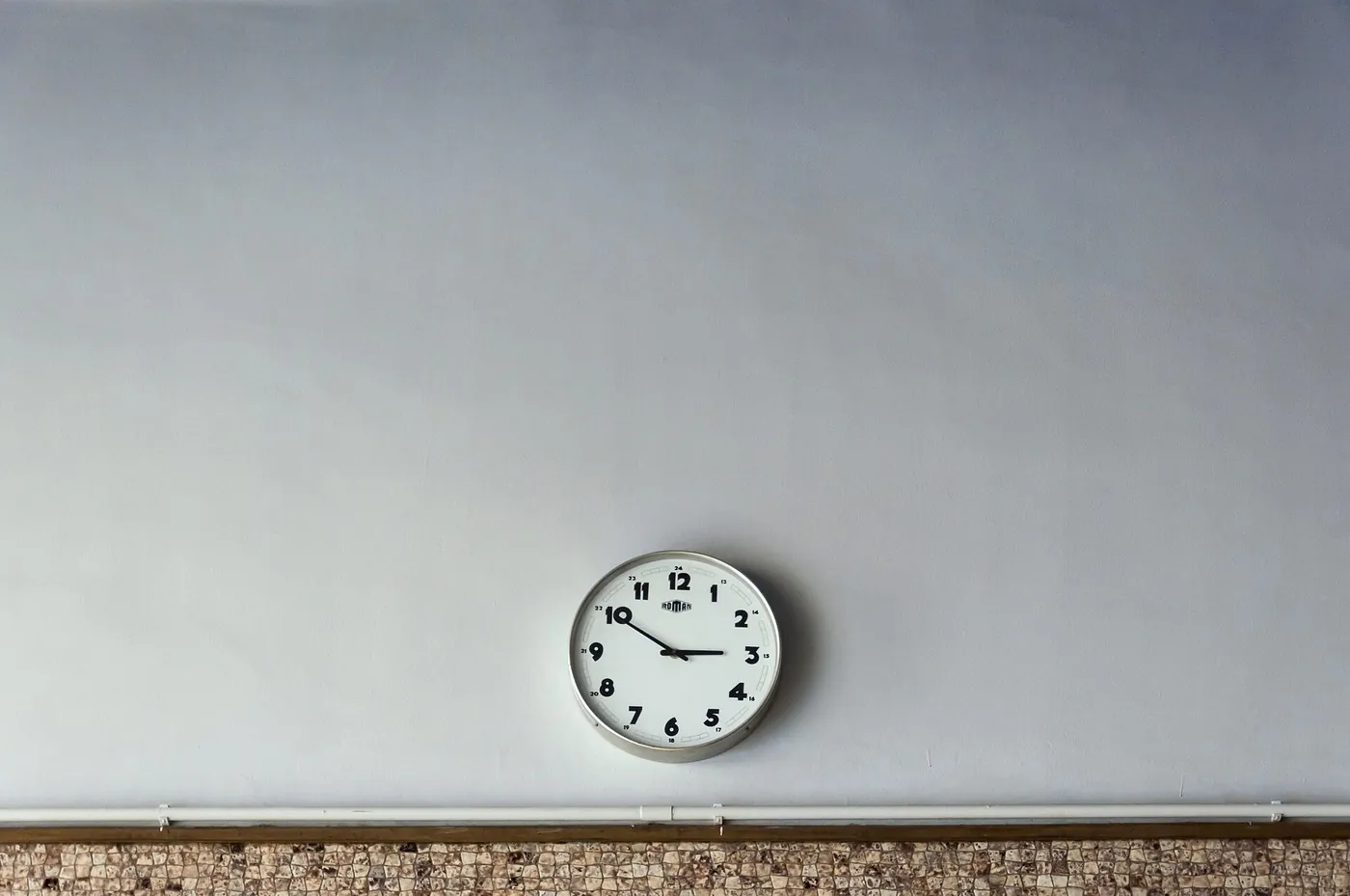 A round analog wall clock with black numerals on a pale wall.