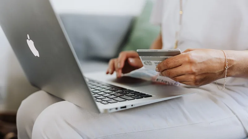 A person holds a payment card while using a laptop.