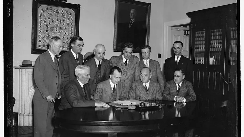 Internal Revenue officials and field agents around a table of papers during a 1937 conference on income-tax audits.